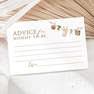 May include: A white card with brown text that reads "Advice for Mommy-to-Be". There are illustrations of a baby onesie, carrots, and baskets of fruit hanging from a string with clothespins.