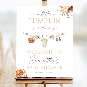 Peut inclure: Panneau de baby shower blanc sur un chevalet en bois, avec le texte "a little PUMPKIN is on the way!" en écriture élégante. Le panneau comprend un panier, des vêtements de bébé et des chaussures de bébé. Les mots "WELCOME TO Samantha's BABY SHOWER" sont également affichés.
