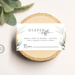 May include: A white card with green foliage and gold glitter accents. The text reads "DIAPER raffle" and "BRING A PACK OF DIAPERS - ANY SIZE, FOR A CHANCE TO WIN A PRIZE!" with a blank line for a name.