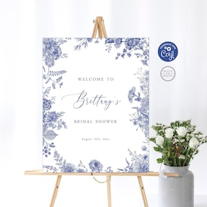 Puede incluir: Un cartel de bienvenida blanco con un borde floral azul y el texto "Bienvenido al Bridal Shower de Brittany el 10 de agosto de 20xx".