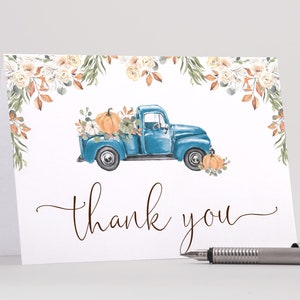 Può includere: Biglietto di ringraziamento ad acquerello con un camion blu vintage pieno di zucche e fiori. La carta ha le parole "thank you" in corsivo. L'immagine è circondata da elementi floreali.
