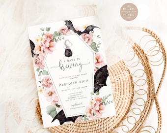Puede incluir: Una tarjeta de invitación rectangular para baby shower con un marco en forma de ataúd, ilustraciones de flores rosas y alas de murciélago negras. El texto dice A BABY IS BREWING, junto con los detalles del evento.