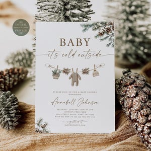 May include: A white baby shower invitation card featuring the text BABY it's cold outside, with a watercolor illustration of baby clothes and pine branches hanging on a string. The card includes details for Annabell Johnson on January 15th.