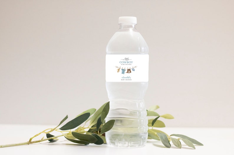 May include: A clear plastic water bottle with a white label that says "Little Cowboy is on the way" with a line drawing of baby clothes hanging on a clothesline. The label also says "[Name]'s Baby Shower".