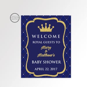 May include: A blue and gold welcome sign for a baby shower. The sign features a gold crown and the text "Welcome Royal Guests to Mary & Matthew's Baby Shower April 22, 2017".