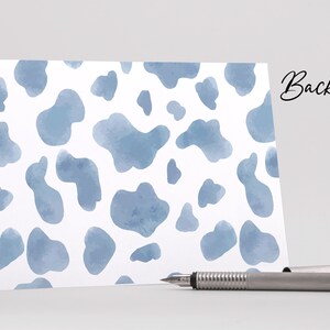 May include: A white card with a blue watercolour cow print pattern. The back side of the card is blank.