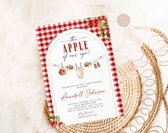 May include: A rectangular baby shower invitation card featuring a red and white gingham border. The center displays an arched design with the text The Apple of our eye!, a clothesline illustration with a onesie, and event details for Annabell Johnson.
