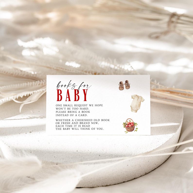 Op de afbeelding: Een witte kaart met de tekst "Books for Baby" in rode en zwarte letters. De kaart bevat illustraties van babyschoentjes, een romper en een mand met appels. De tekst vraagt om een boek in plaats van een kaart.