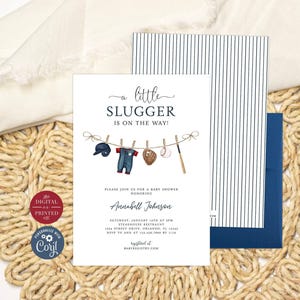 May include: A white baby shower invitation card featuring the text A LITTLE SLUGGER IS ON THE WAY! and an illustration of baseball gear hanging on a clothesline. The set includes a matching envelope with black vertical stripes and a solid navy blue flap.