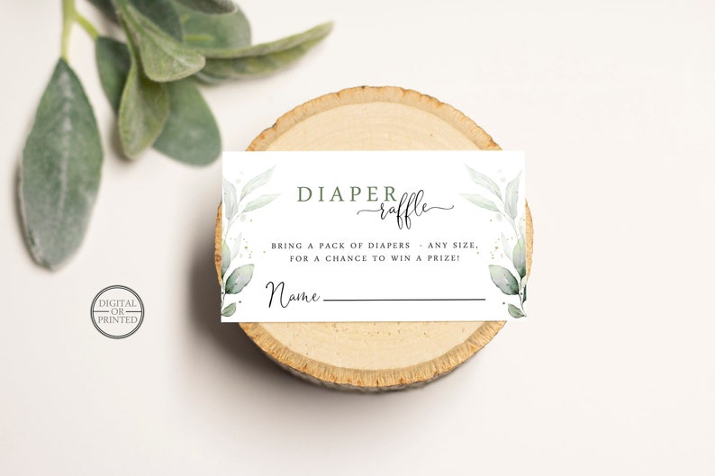 May include: A white card with green foliage and gold glitter accents. The text reads "DIAPER raffle" and "BRING A PACK OF DIAPERS - ANY SIZE, FOR A CHANCE TO WIN A PRIZE!" with a blank line for a name.
