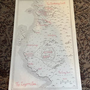 Op de afbeelding: Een handgetekende fantasiekaart met een beige achtergrond en rode en zwarte inkt details. De kaart toont een kustlijn, bergen en diverse plaatsnamen, waaronder "The Zeyaren Sea" en "The Long Road". Een schaal in mijlen is inbegrepen.