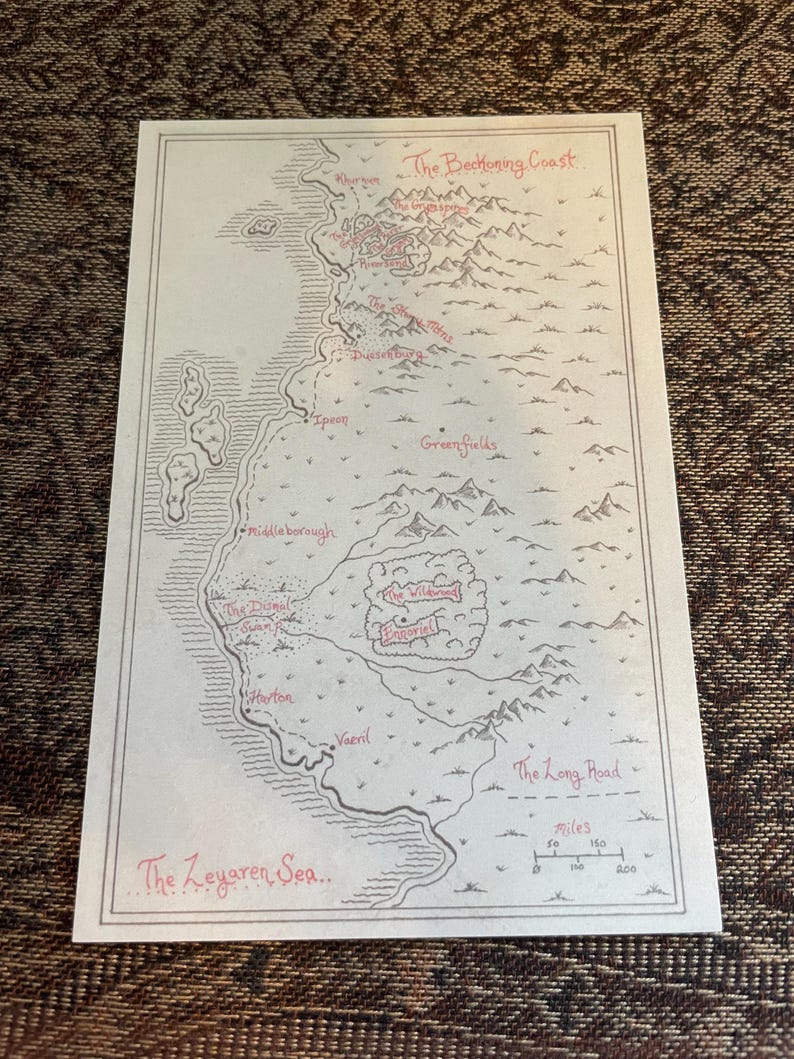 Op de afbeelding: Een handgetekende fantasiekaart met een beige achtergrond en rode en zwarte inkt details. De kaart toont een kustlijn, bergen en diverse plaatsnamen, waaronder "The Zeyaren Sea" en "The Long Road". Een schaal in mijlen is inbegrepen.