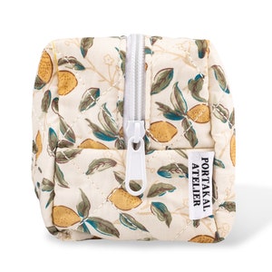 May include: A white quilted makeup bag with a zipper closure and a lemon print. The bag has a label that says "PORTAKAL ATELIER".