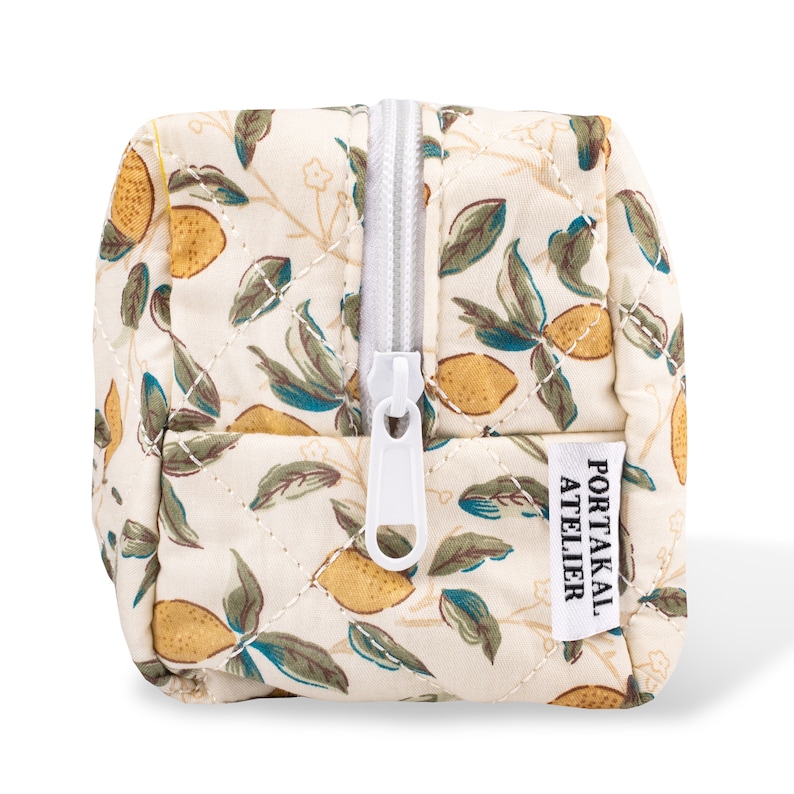 May include: A white quilted makeup bag with a zipper closure and a lemon print. The bag has a label that says "PORTAKAL ATELIER".