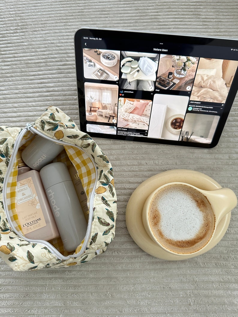 May include: A white and yellow floral patterned toiletry bag with a zipper closure. The bag is open and contains three bottles of toiletries. The bottles are labeled "Neroli & Orchidee", "L'Occitane", and "rhode".