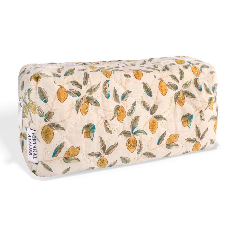 May include: A white quilted makeup bag with a lemon print. The bag has a zipper closure and a label that reads "PORTAKAL ATELIER".