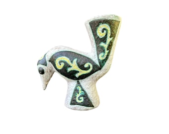 Puede incluir: Una figurita de pájaro de cerámica blanca con detalles pintados en negro, verde y amarillo. El pájaro tiene un cuello largo y curvo y un pequeño pico. La figurita está decorada con un patrón floral estilizado.