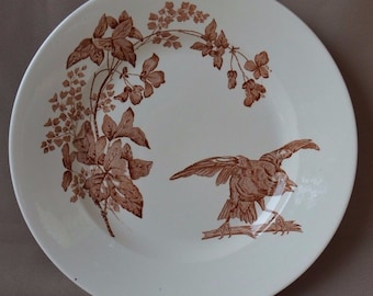 Pode incluir: Um prato de cerâmica branco com um desenho floral castanho e um pássaro castanho empoleirado num ramo. O prato tem uma borda e é decorado com um padrão repetitivo de folhas e flores.