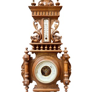 May include: An antique wooden barometer with intricate carvings. The barometer features a circular dial with a detailed illustration and a thermometer. The wooden frame is a warm brown color, with decorative elements.