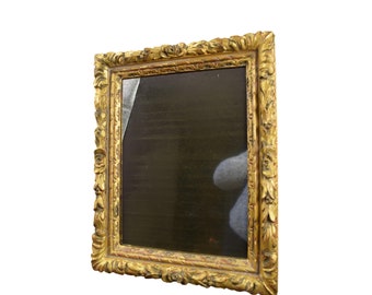 May include: An ornate picture frame in a gold colour with a dark background inside. The frame has a detailed design with intricate carvings.