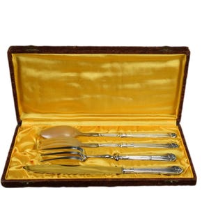 May include: A set of silver cutlery in a brown velvet lined box. The set includes a knife, fork, and spoon.