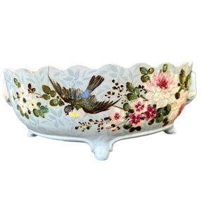 Puede incluir: Un cuenco de cerámica azul claro con tres patas, que presenta un diseño pintado a mano de flores rosas y blancas y un pájaro azul.
