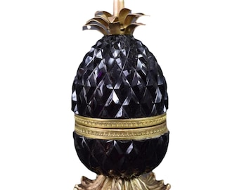 May include: A black glass pineapple shaped trinket box with gold accents and a hinged lid. The box sits on a gold metal base.