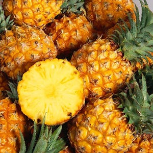 May include: A close-up of a group of ripe pineapples. The pineapples are yellow and have a rough, textured skin. Some of the pineapples are cut in half, revealing the juicy, yellow flesh.
