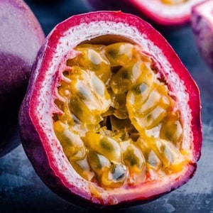 May include: A halved passion fruit with a vibrant purple exterior and a bright yellow interior filled with seeds. The fruit is cut open, revealing the juicy pulp and seeds.