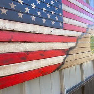 May include: Wooden American flag with red and white stripes and a blue field with white stars. The flag has a distressed look and features the John Deere logo in the lower right corner.