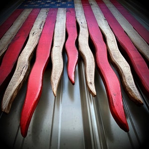 May include: A wooden American flag with red, white and blue stripes. The flag is cut into points, creating a unique and decorative design.