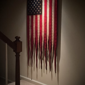 May include: A distressed American flag with red, white and blue stripes and stars. The flag is hanging on a wall and the stripes are dripping down like melted wax.
