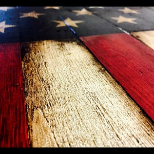 May include: Close-up of a wooden American flag with red, white and blue paint. The flag is made from reclaimed wood and has a distressed look.