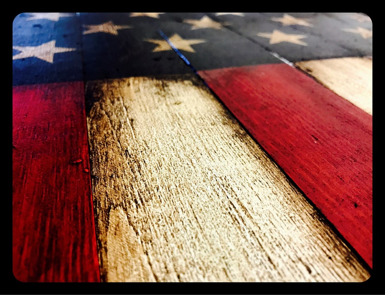 May include: Close-up of a wooden American flag with red, white and blue paint. The flag is made from reclaimed wood and has a distressed look.