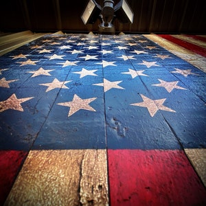 May include: A wooden American flag painted in red, white and blue. The flag is made of weathered wood planks and has a distressed look. The stars are white and the stripes are red and white.