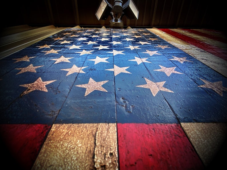 May include: A wooden American flag painted in red, white and blue. The flag is made of weathered wood planks and has a distressed look. The stars are white and the stripes are red and white.