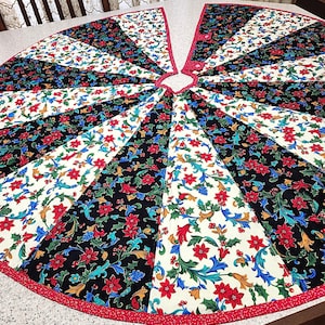 May include: A circular quilted tree skirt featuring alternating wedge-shaped panels of black and cream fabric. Both patterns display a vibrant floral motif with red poinsettias, green holly leaves, and blue accents. The edge is finished with red trim.