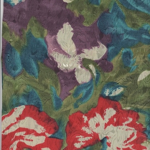 May include: A fabric with a floral pattern in shades of red, white, green, blue, and purple. The fabric has a textured surface.