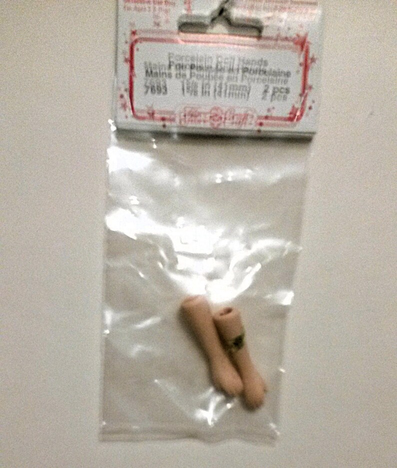 May include: Two porcelain doll hands in a clear plastic bag. The bag has a label that reads "Porcelain Doll Hands, Mains de Poup&eacute;e en Porcelaine, 5683, 1 1/8 in (31mm), 2 pcs".