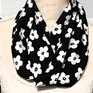 May include: A black infinity scarf with a white floral pattern. The scarf is made of a soft, comfortable fabric and is perfect for adding a touch of style to any outfit.