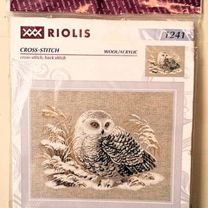 May include: A cross-stitch kit featuring a detailed image of a white owl in a snowy landscape. The kit includes the text "RIOLIS", "CROSS-STITCH", and "WOOL/ACRYLIC". The finished design measures 17¾" x 13¾".