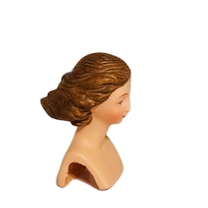 May include: A ceramic bust of a woman with brown hair, the bust is painted with a light skin tone and the hair is painted brown.