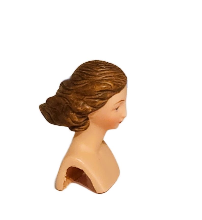 May include: A ceramic bust of a woman with brown hair, the bust is painted with a light skin tone and the hair is painted brown.