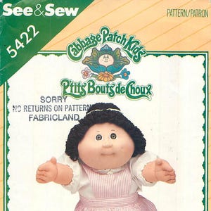 May include: A See & Sew 5422 Cabbage Patch Kids sewing pattern envelope featuring a doll with black yarn hair, a white blouse, and a pink and white striped pinafore. The packaging includes the text Cabbage Patch Kids and P'tits Bouts de Choux.