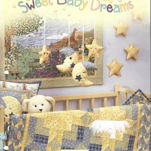 May include: A nursery scene with a crib, quilt, and decorative elements. The quilt features yellow and blue patchwork. Hanging are star and moon-shaped plushies. The text "Sweet Baby Dreams" is displayed above the crib, with the Debbie Mumm logo.