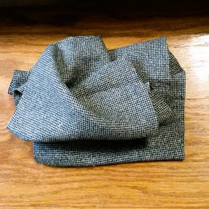 May include: A gray and white patterned fabric folded into a square shape. The fabric has a subtle texture and a geometric design.