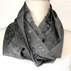 May include: A gray silk scarf with a delicate floral pattern. The scarf is folded and draped around a mannequin's neck.