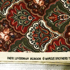 May include: Close-up of a fabric with a paisley pattern in shades of red, green, and brown. The design includes floral and paisley motifs. The fabric has a cream-colored border with the text "FAYE LIVERMAN BURGOS © MARCUS BROTHERS".