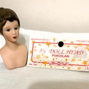 May include: A porcelain doll head with brown hair, a white bust, and a label that reads "3/4 Doll Head Porcelain Fibre-Craft No. 7691 1Pc".
