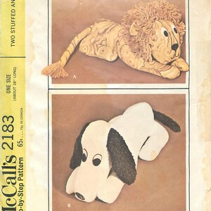 May include: A vintage McCall's pattern for two stuffed animals: a lion and a dog. The lion is tan with a brown mane and the dog is white with black ears. The pattern is labeled "One Size (About 18" Long)".